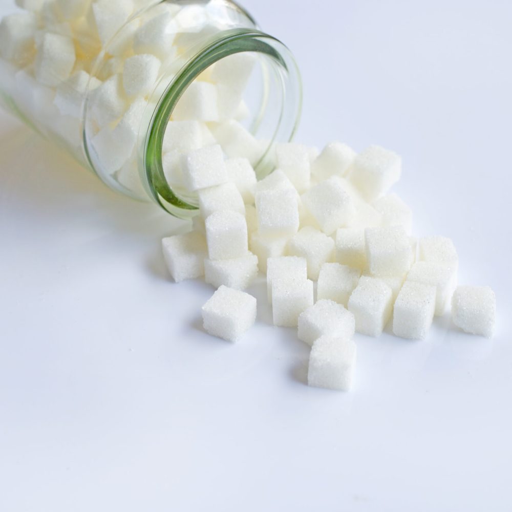 Glass bottle of sugar cubes on white background